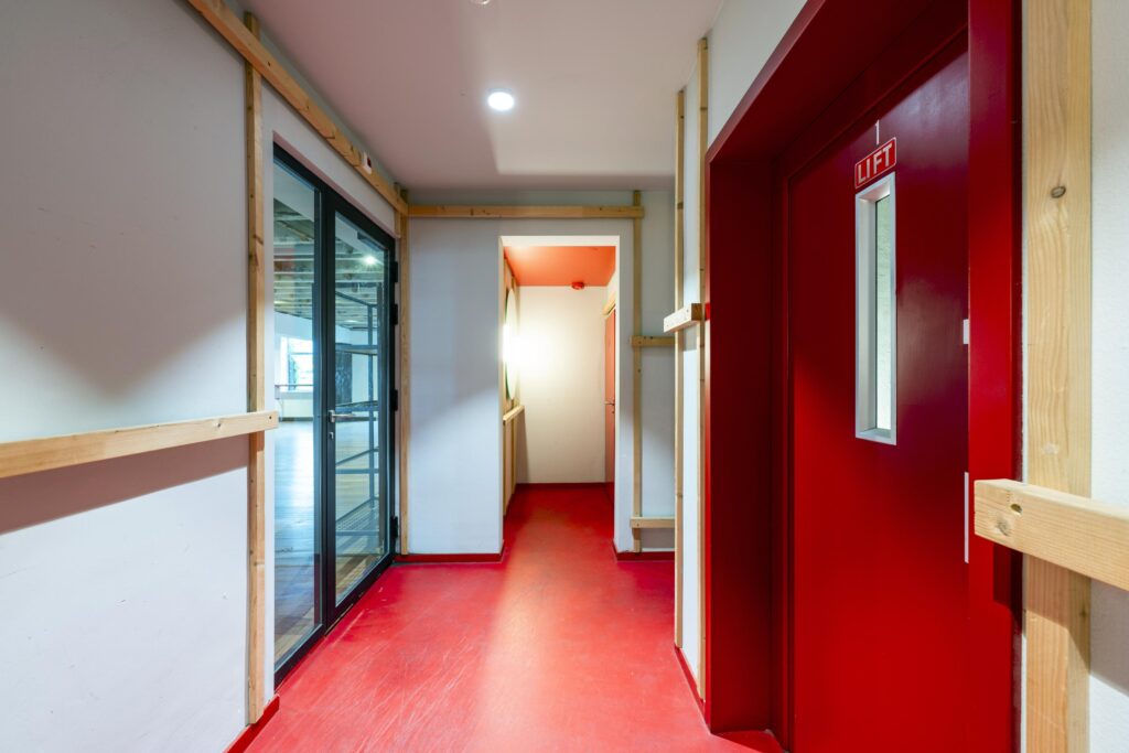 Hal met rode vloer en rode liftdeur in een modern kantoorgebouw aan de De Ruijterkade.